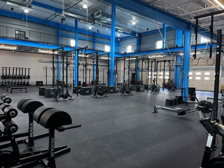 Empty gym with weight racks, dumbbells, and pull-up rigs in a spacious industrial-style workout area.