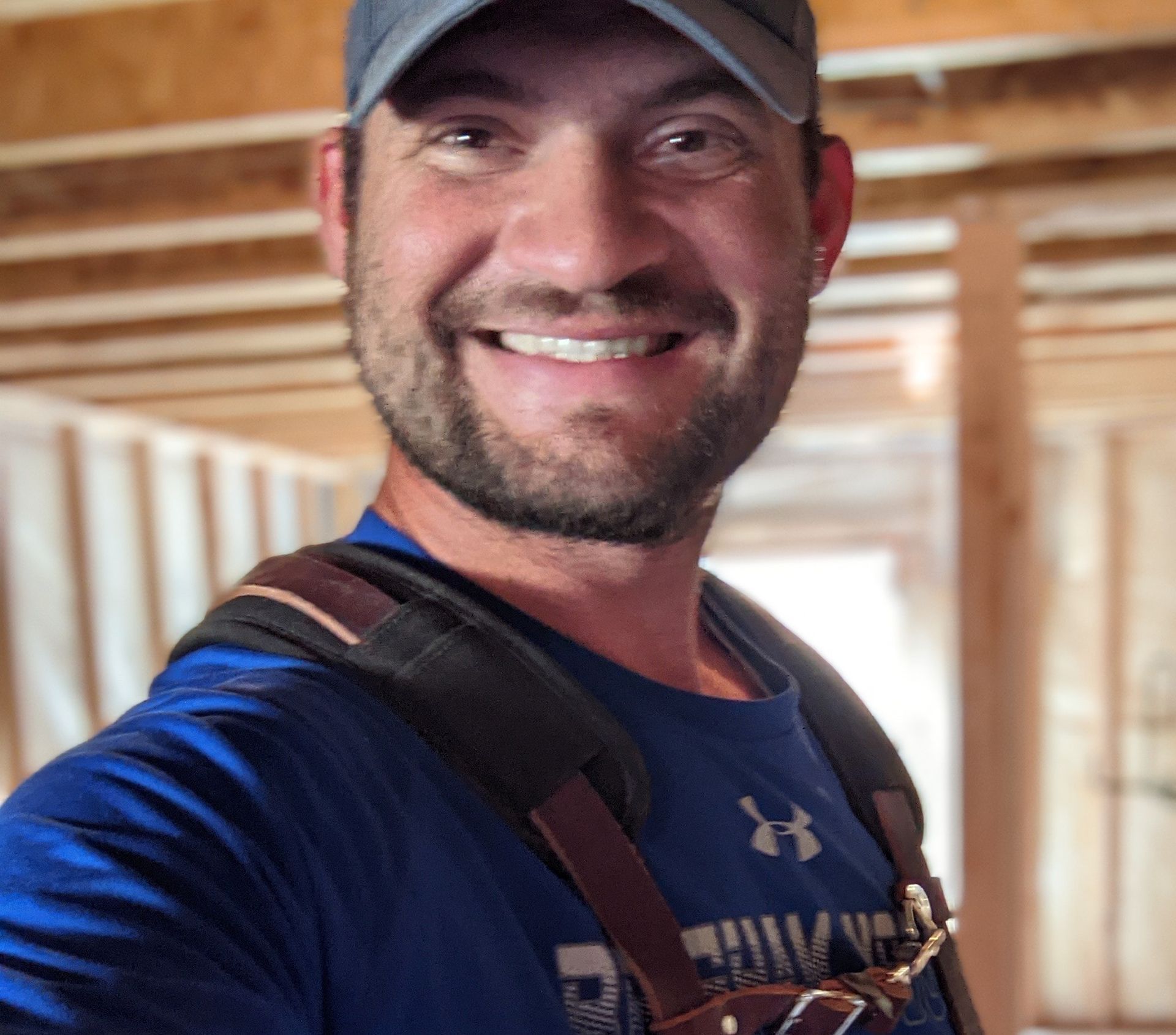 A man wearing a hat and suspenders is smiling for the camera