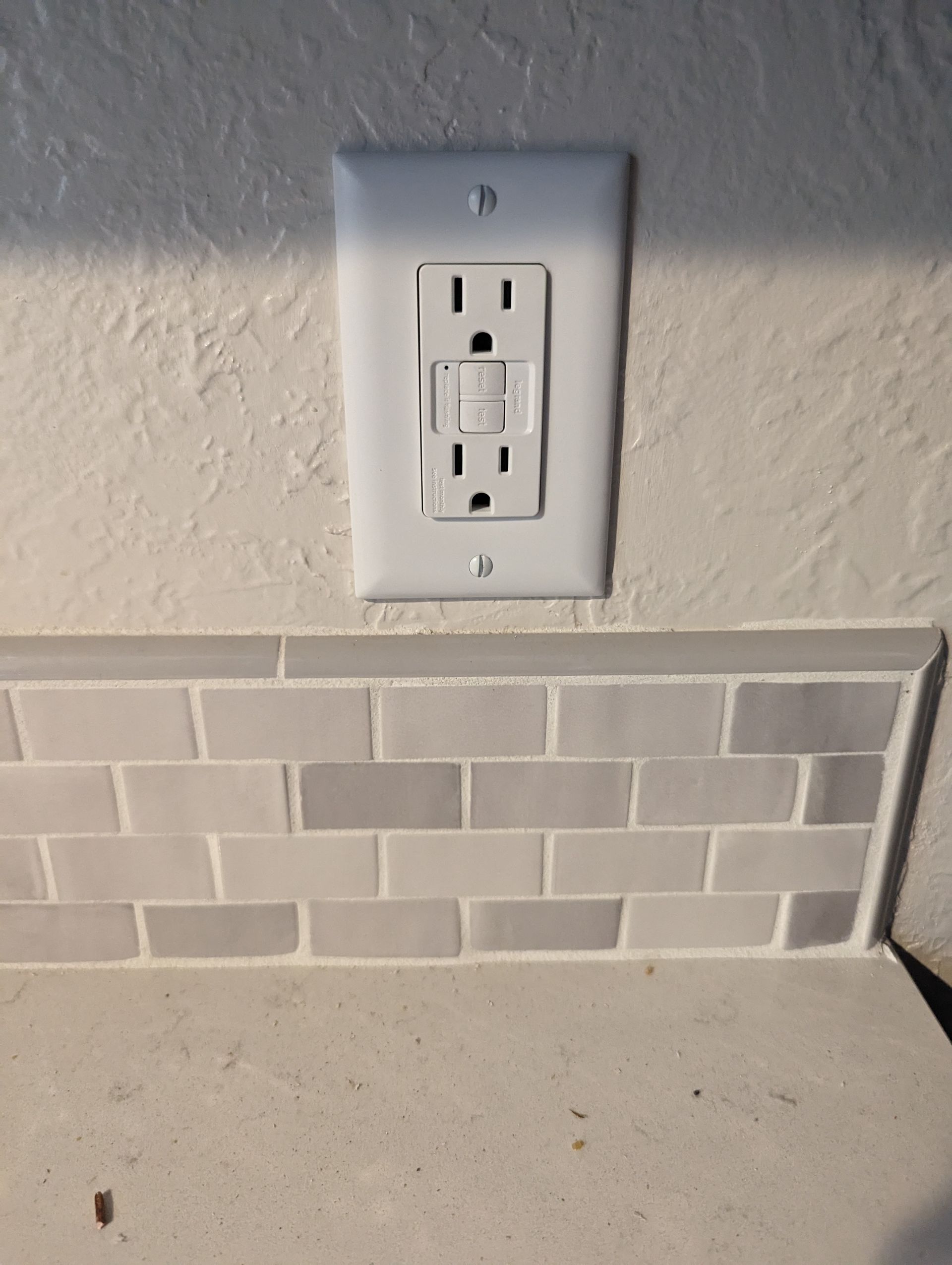 A white electrical outlet is sitting on a tiled wall.