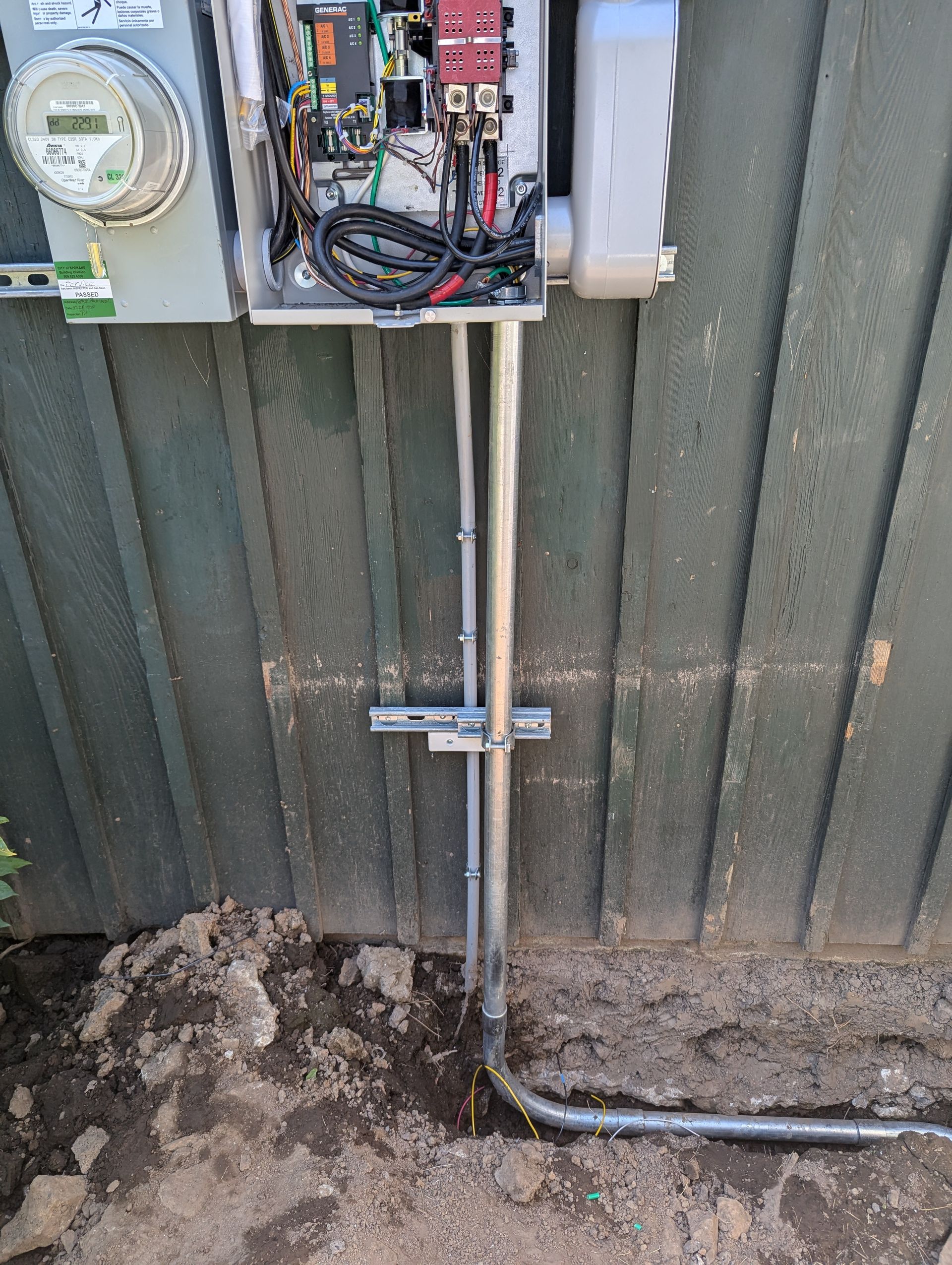 A electrical box is sitting on the side of a building next to a fence.