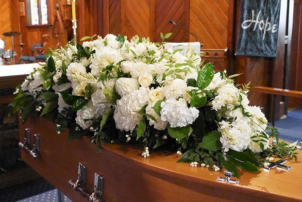 A Coffin is Decorated With White Flowers in a Church — Hutchinson Family Funerals In Taree, NSW