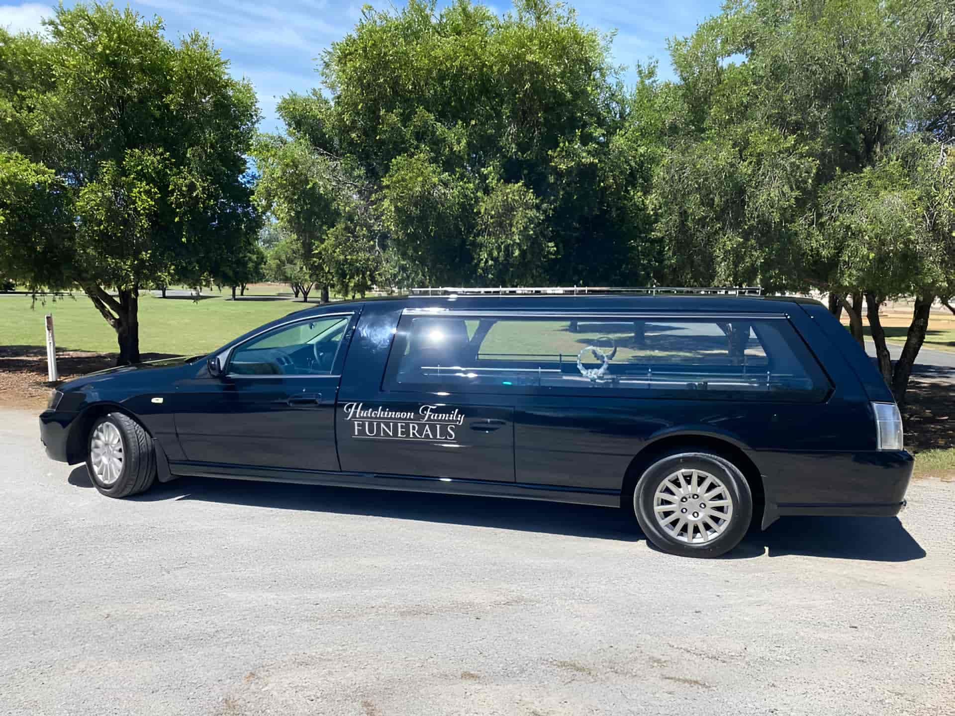 A Black Limousine is Parked in a Parking Lot in Front of Trees — Hutchinson Family Funerals In Taree, NSW