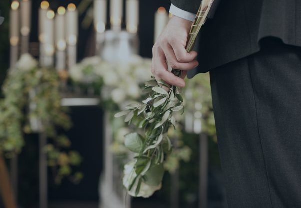 A Man in a Suit is Holding a Bouquet of Flowers at a Funeral — Hutchinson Family Funerals In Taree, NSW