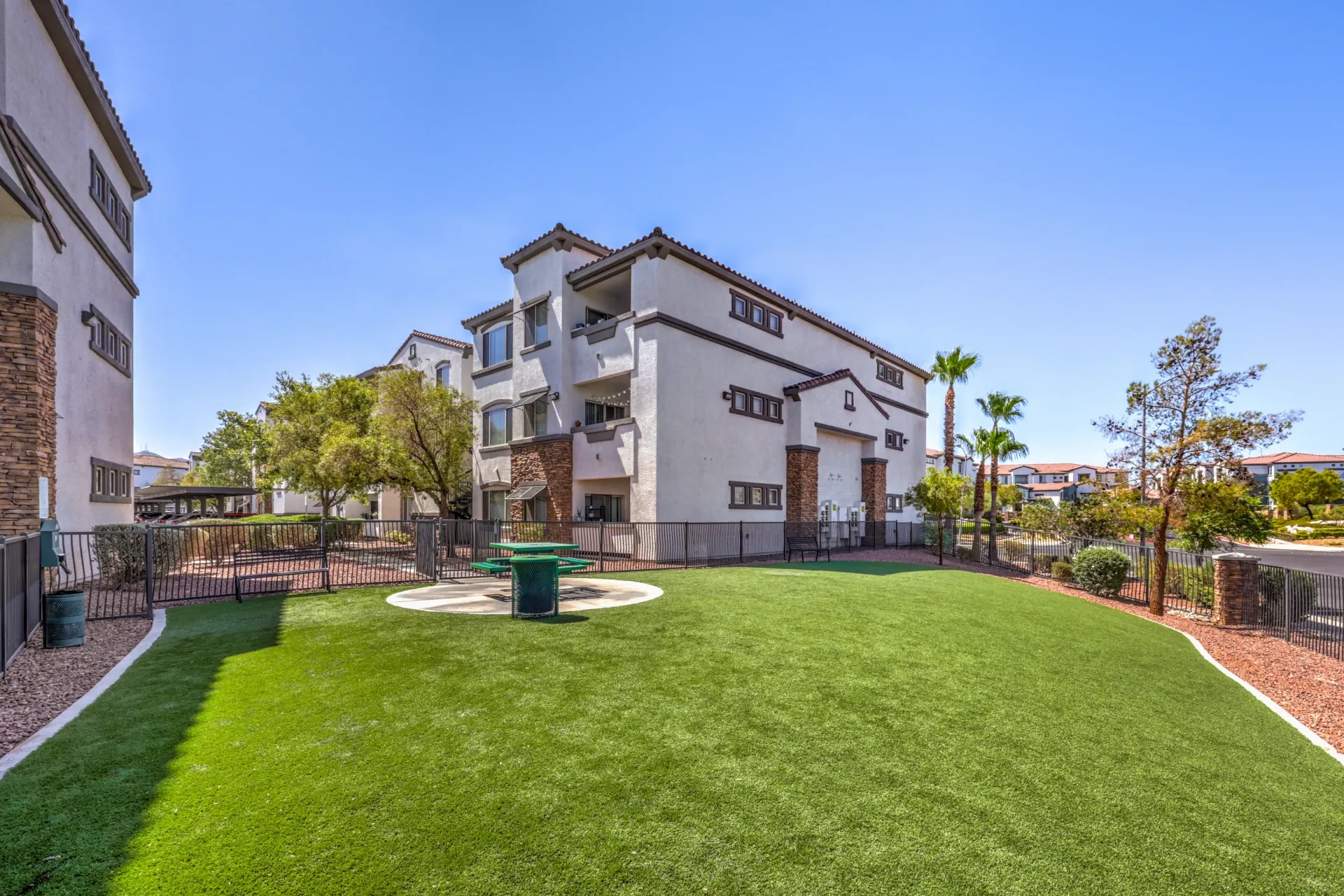 Outdoor green space with a picnic table and benches, adjacent to apartment buildings at Cornerstone Park in Henderson, NV.