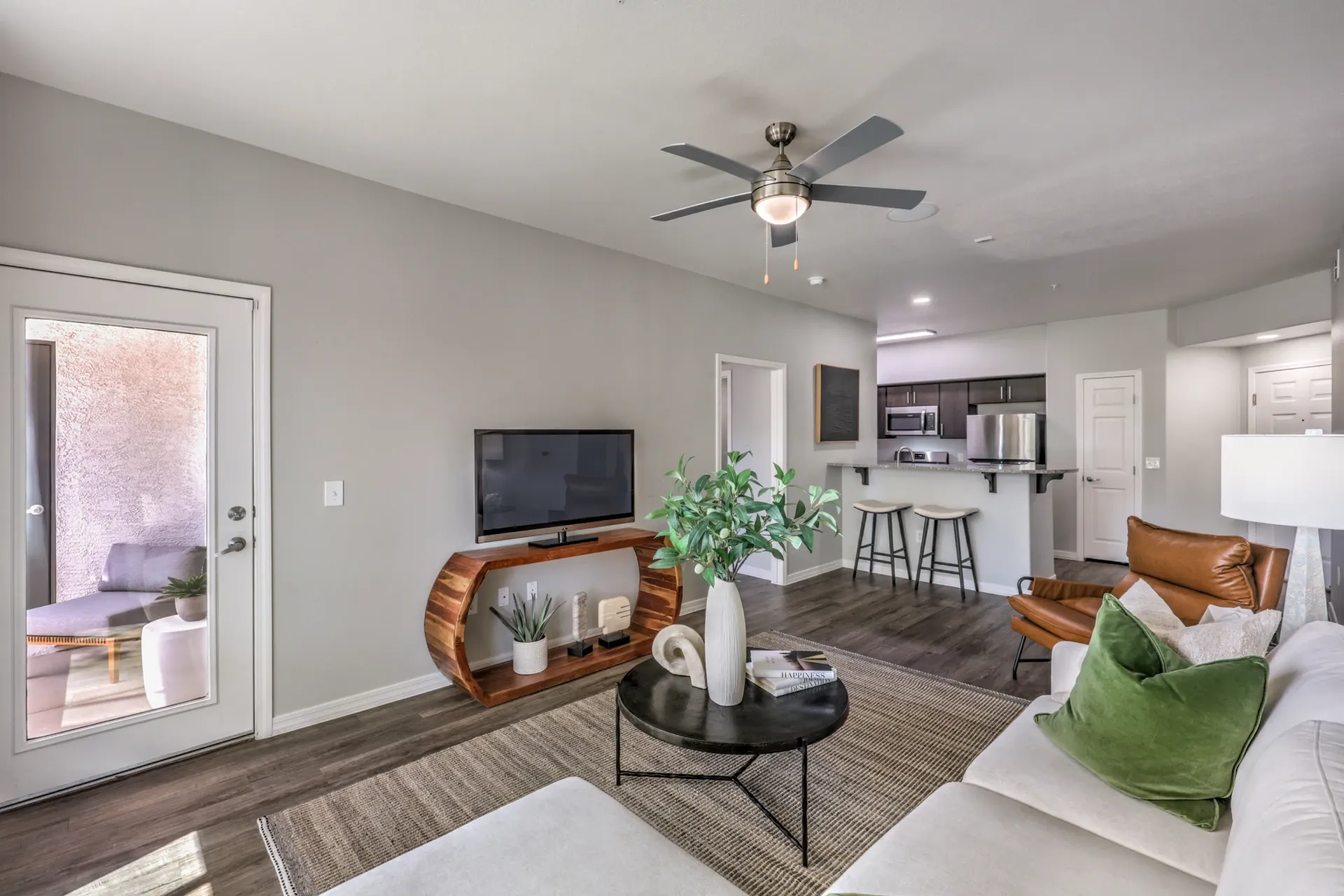 Living room and open kitchen area with island seating and a TV at Cornerstone Park in Henderson, NV.