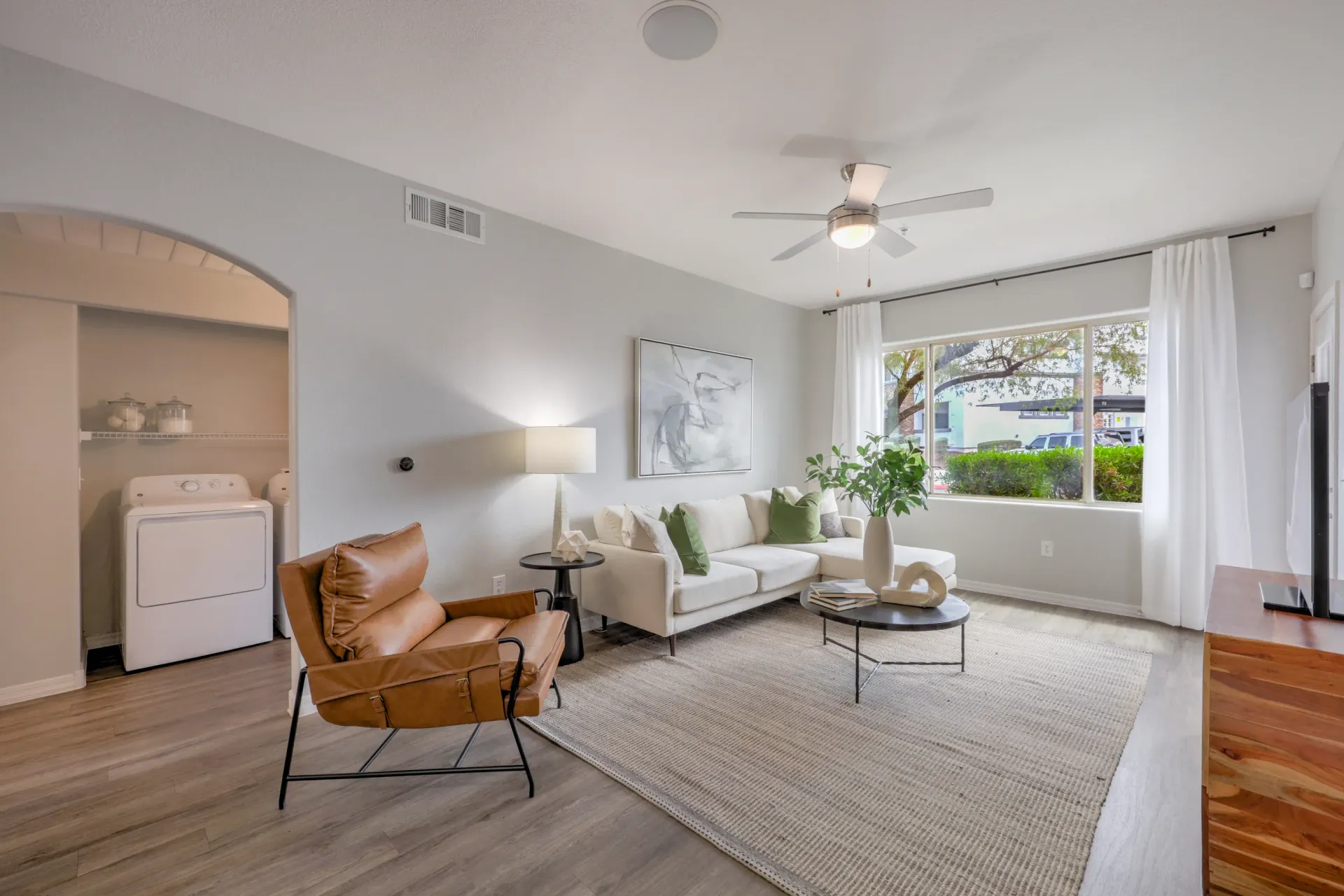 Living room with a sectional sofa, armchair, coffee table, and laundry area at Cornerstone Park in Henderson, NV.