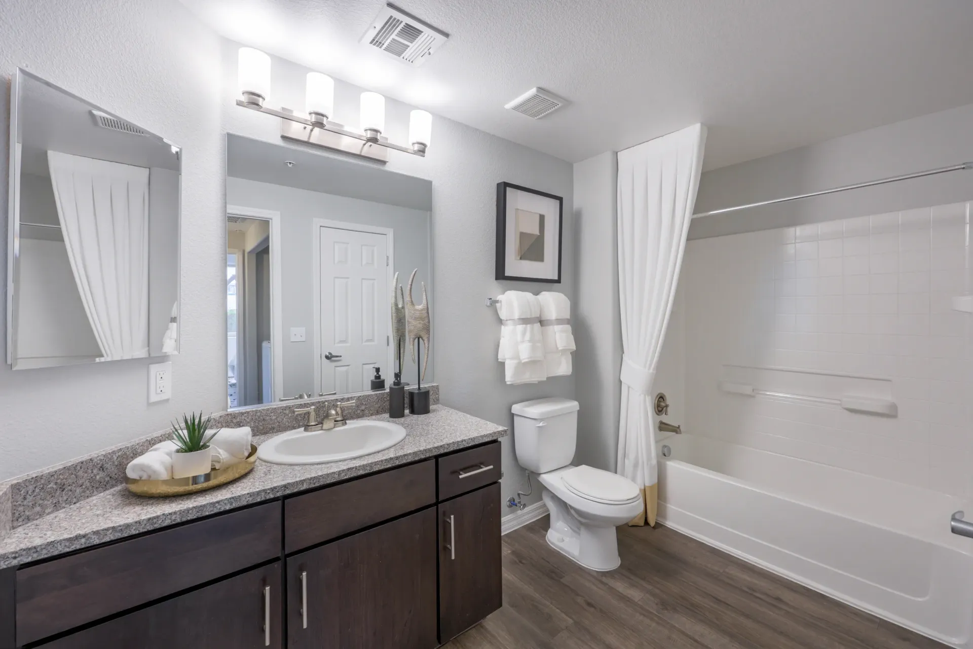 Modern bathroom with a dark wood vanity, granite countertop, white sink, toilet, and a white bathtub with a shower curtain at Cornerstone Park in Henderson, NV.