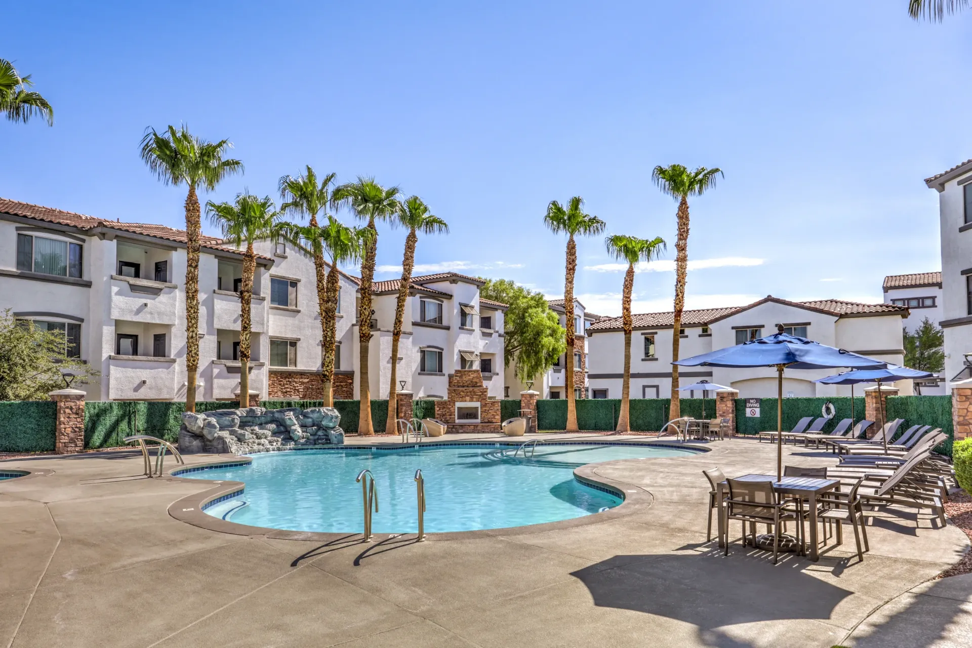Resort-style swimming pool with lounge chairs and umbrellas, surrounded by palm trees and apartment buildings at Cornerstone Park in Henderson, NV.