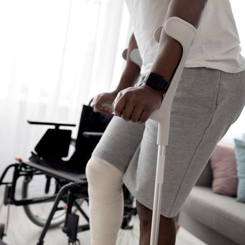 Personal Injury A man with a cast on his leg is standing with crutches in front of a wheelchair.