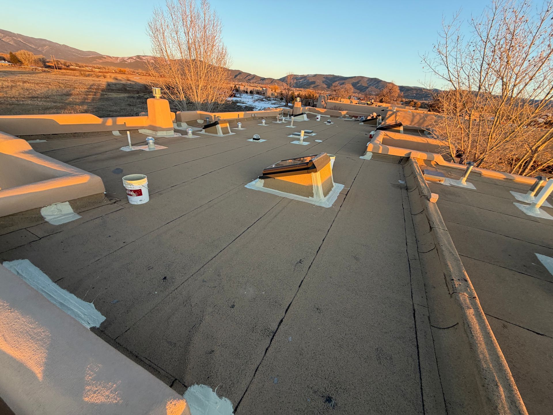 Flat roof with several vents and chimneys, surrounded by a mountain landscape at sunset.