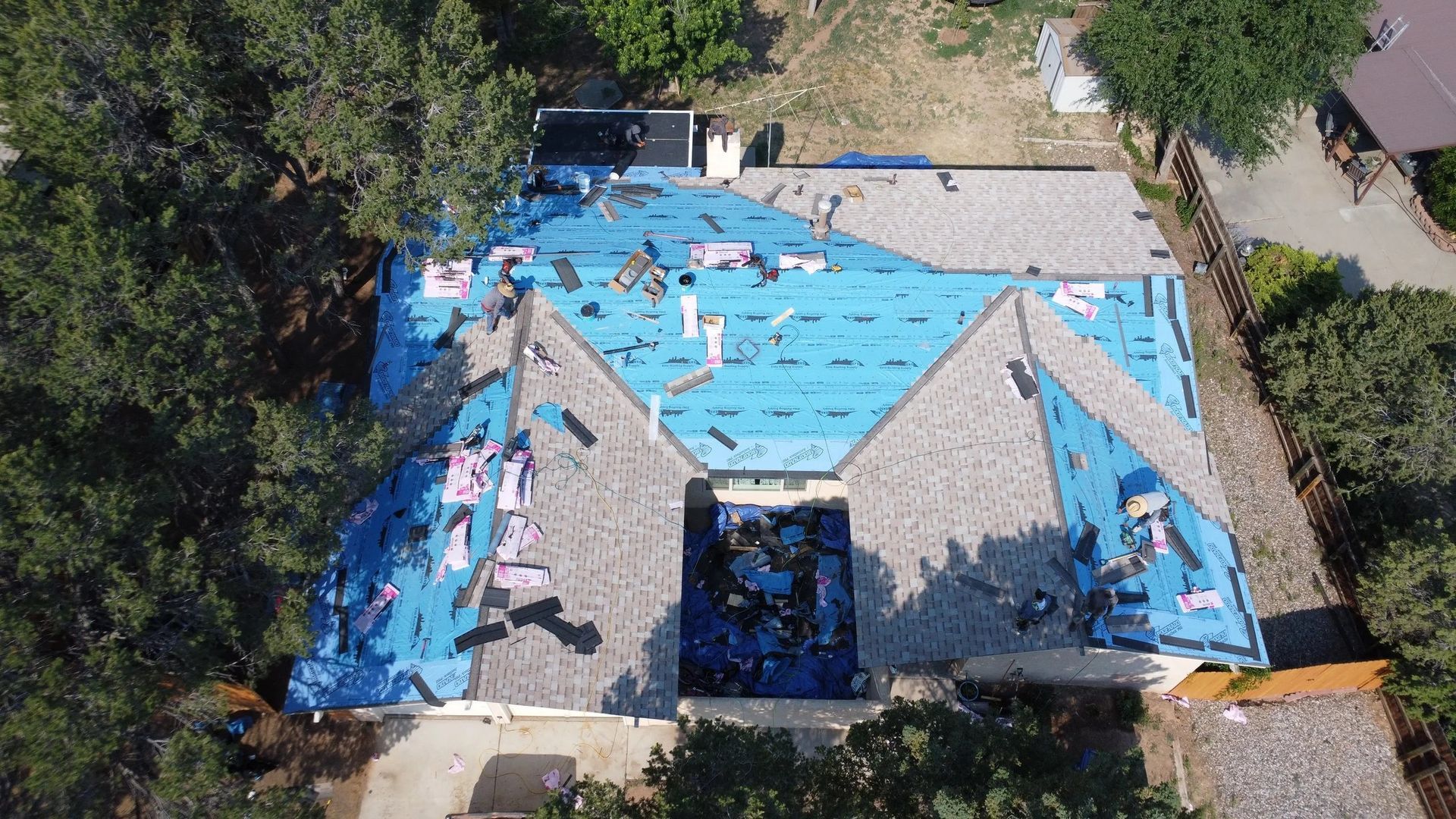 Roof partially covered with blue underlayment and brown shingles; construction in progress.