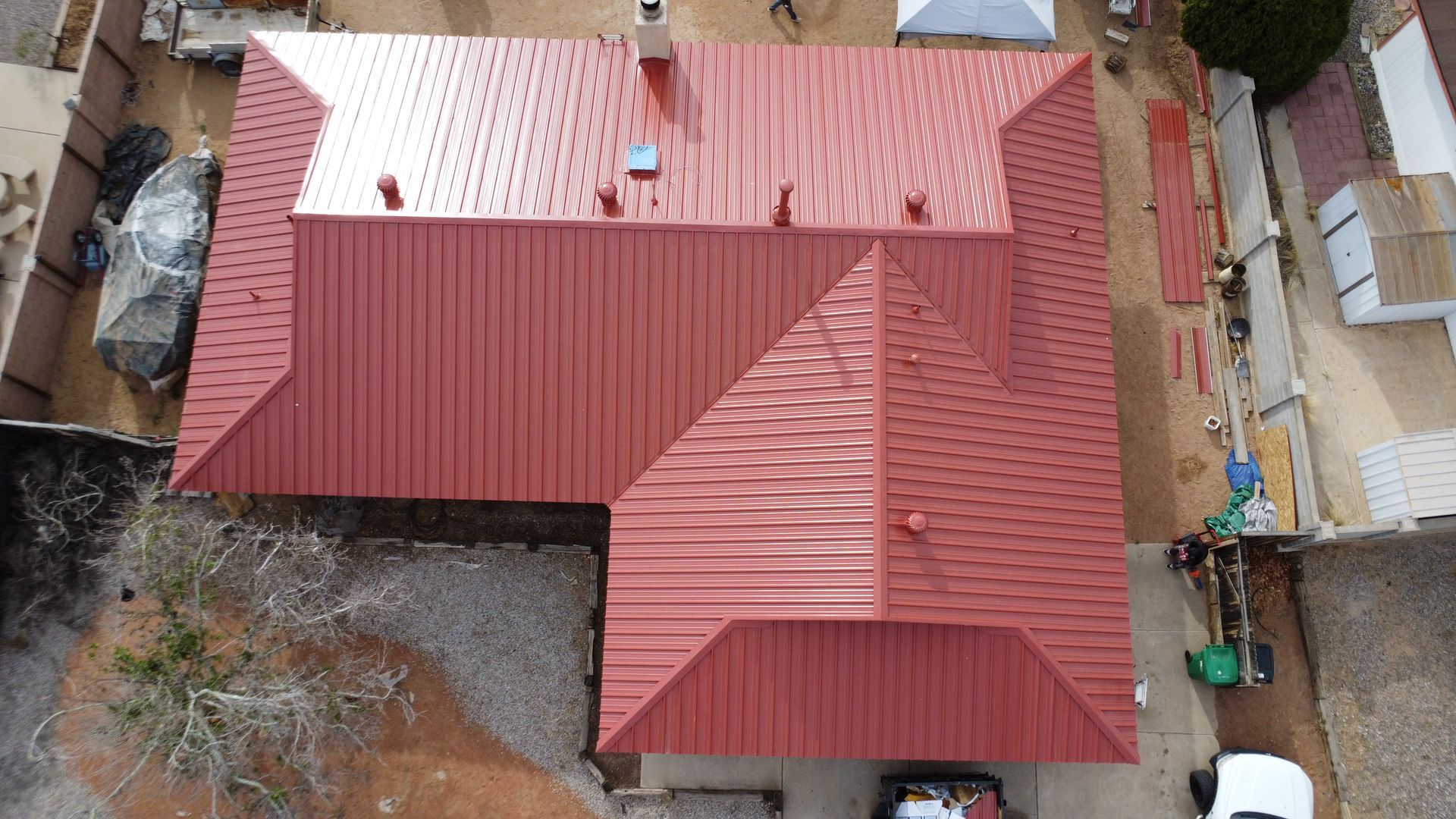 Workers installing a metal roof on a small building. Bright sunlight, outdoor setting.