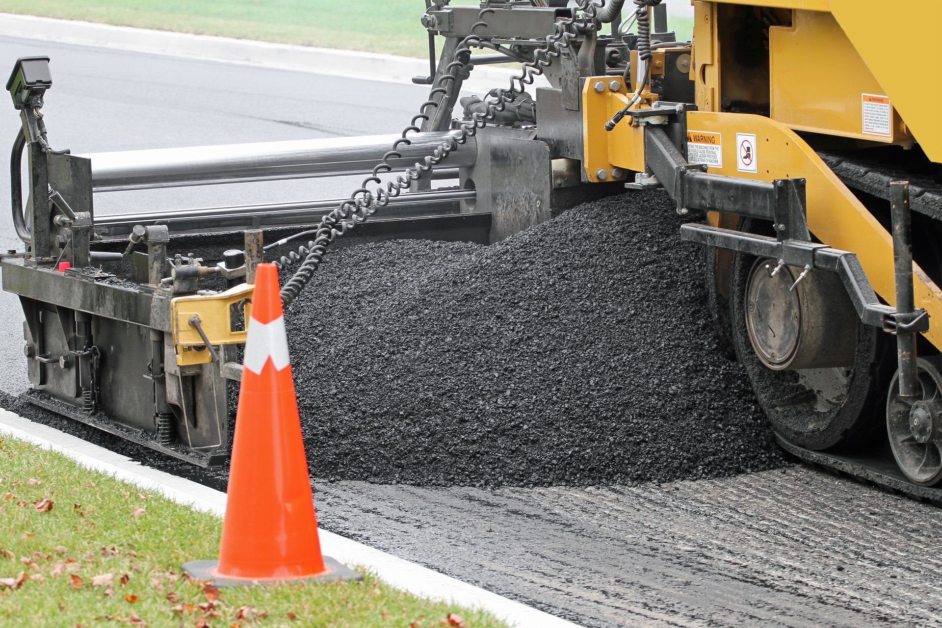 View of an asphalt paving machine at work, spreading asphalt for a new road surface. View of an asphalt paving machine at work, spreading asphalt for a new road surface.