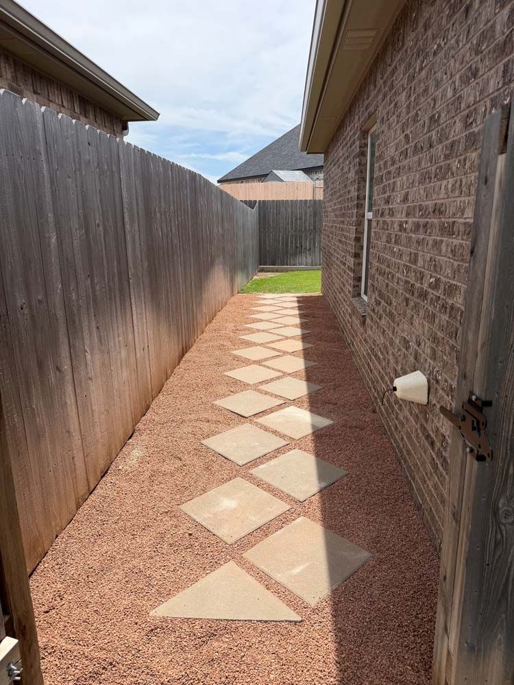 Narrow side yard with diamond stepping stones, red gravel, wooden fence, and brick house wall.