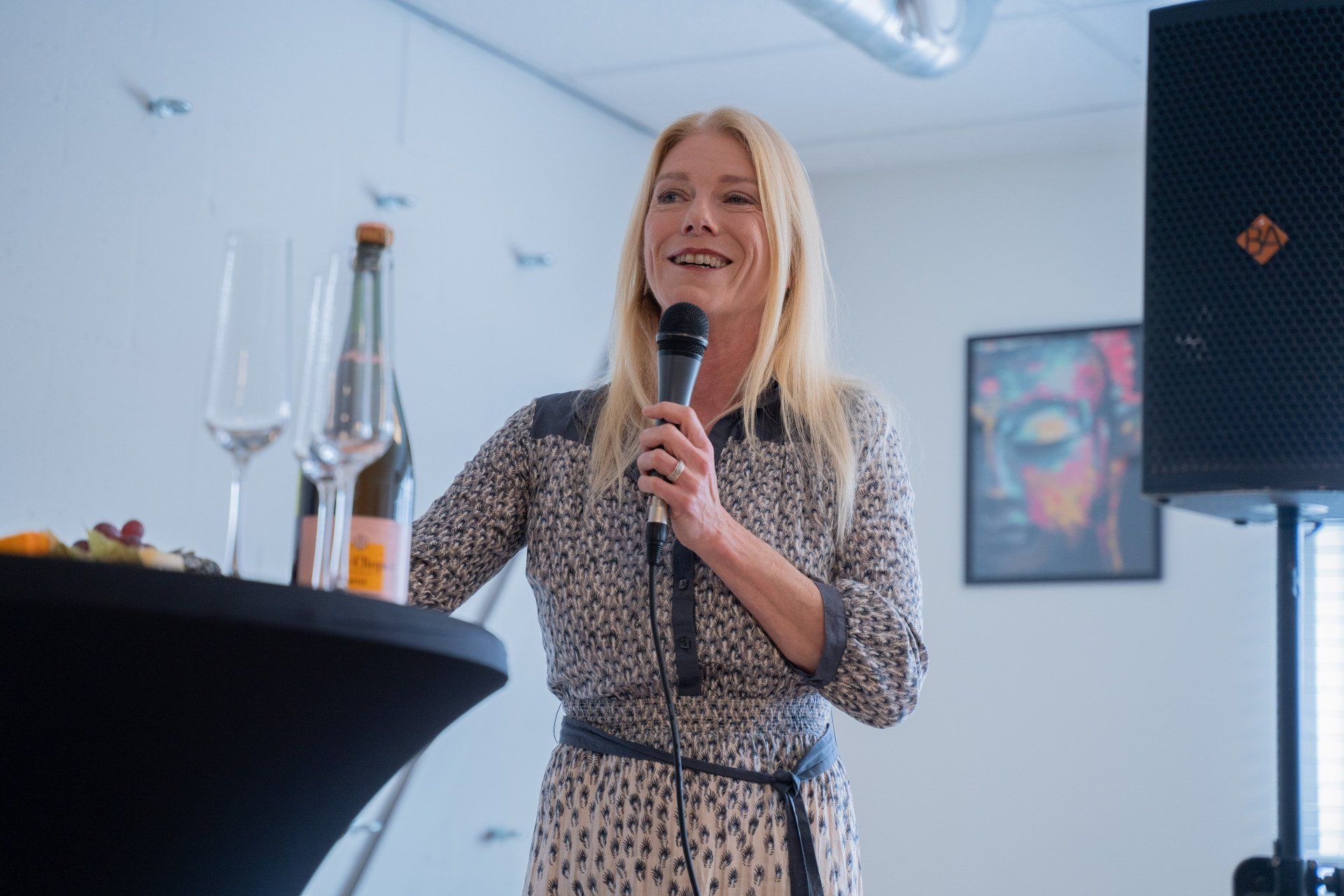 Een vrouw houdt een microfoon vast voor een tafel met wijnglazen en een fles wijn.