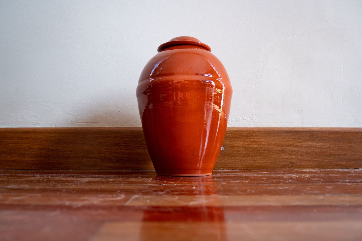 A red vase is sitting on a wooden floor.
