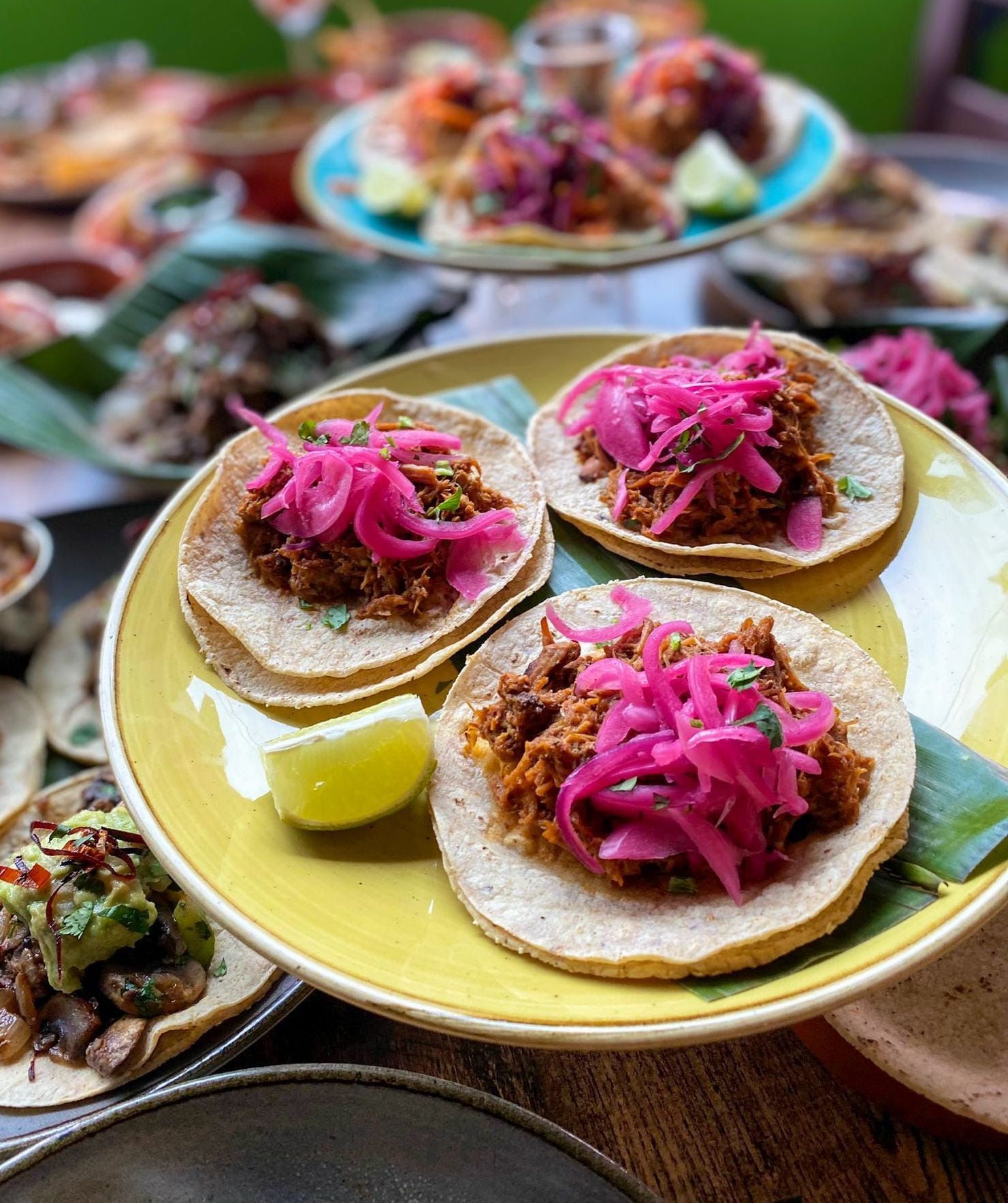 A plate of tacos with pink onions and a lemon on a table.