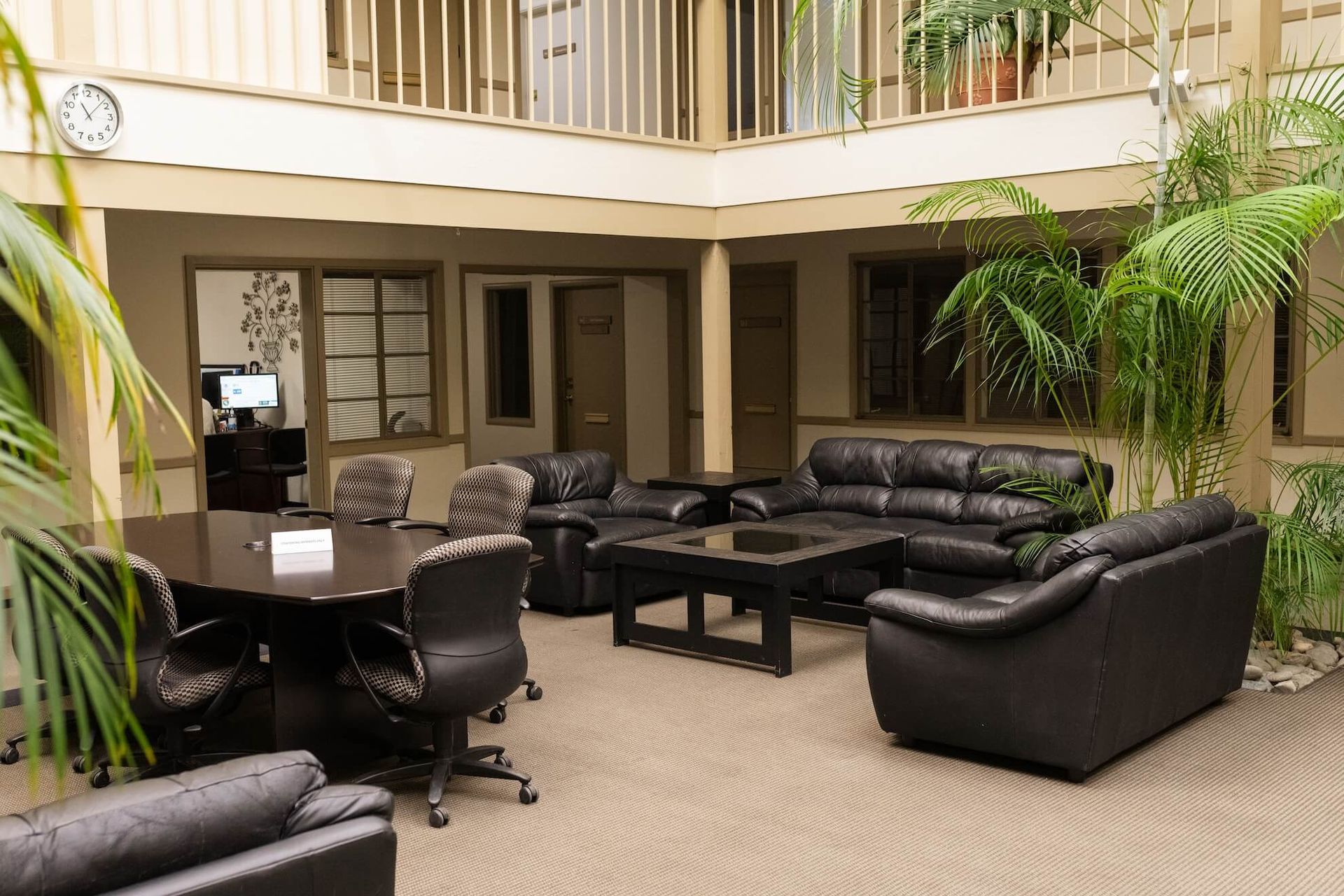Lobby lounge with black leather sofas, chairs, and tables under a second-floor balcony.
