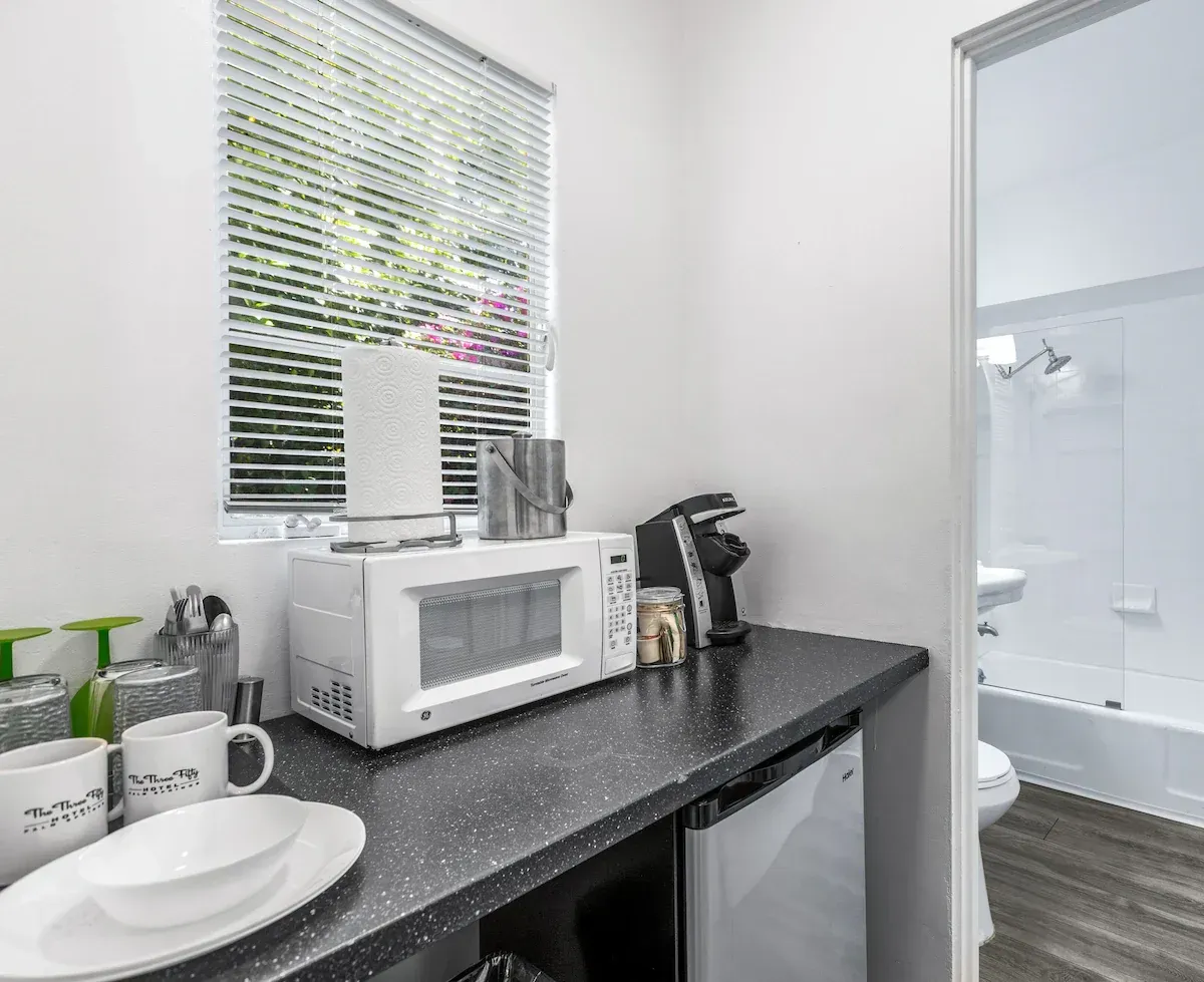 Bathroom vanity with black countertop, microwave, mugs, and a view into the shower area