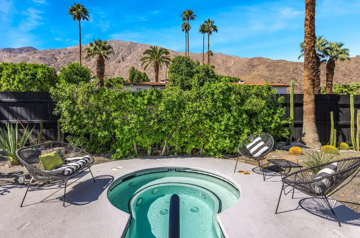 Backyard patio with a small round pool, lounge chairs, palm trees, and desert mountains beyond the hedge