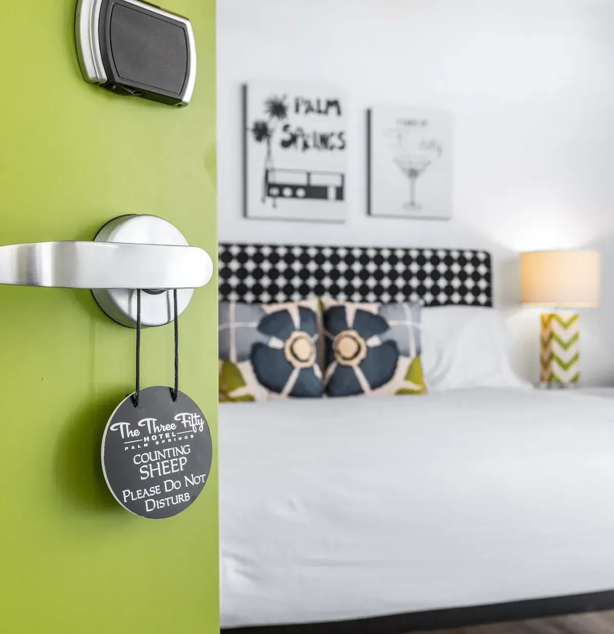 Modern bedroom with white bed, green accent wall, patterned pillows, and a bedside lamp