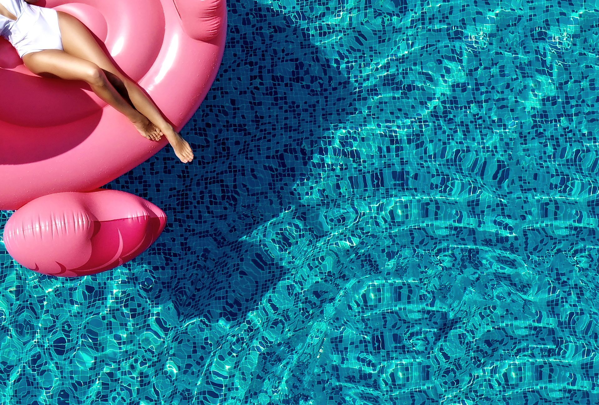 Person relaxing on a pink inflatable float in a bright blue pool