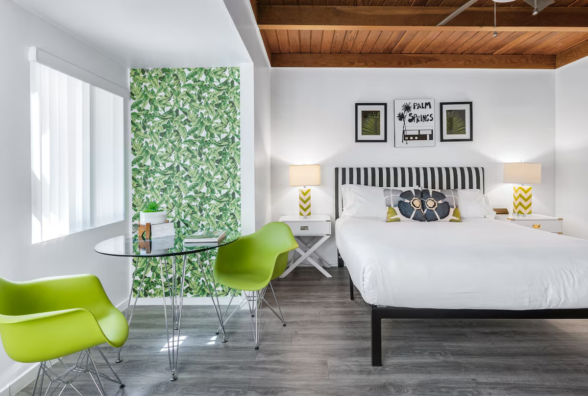 Modern bedroom with white bed, green chairs, glass table, and leafy accent wall