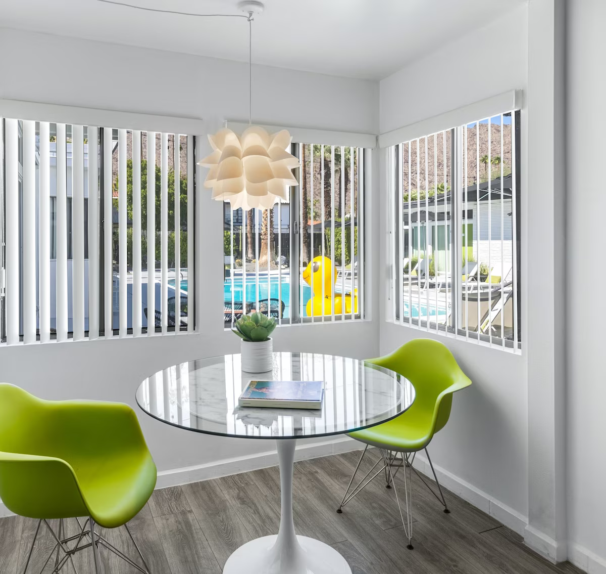 Bright dining nook with lime green chairs, round table, and bay windows overlooking a pool.
