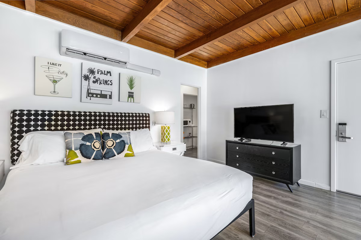 Bright bedroom with a white bed, wood ceiling, wall art, and TV on a black dresser