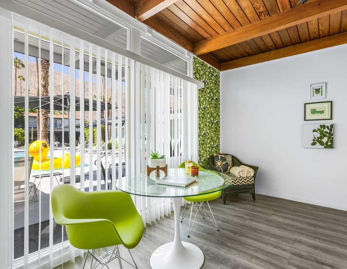 Modern sunroom with green chairs, glass table, vertical blinds, and wood ceiling paneling