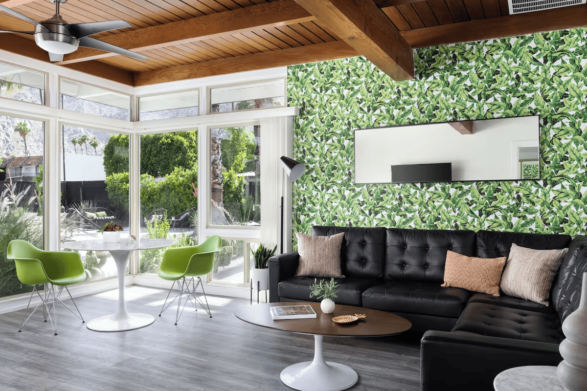 Modern patio living room with black sectional, green chairs, and leafy wall decor