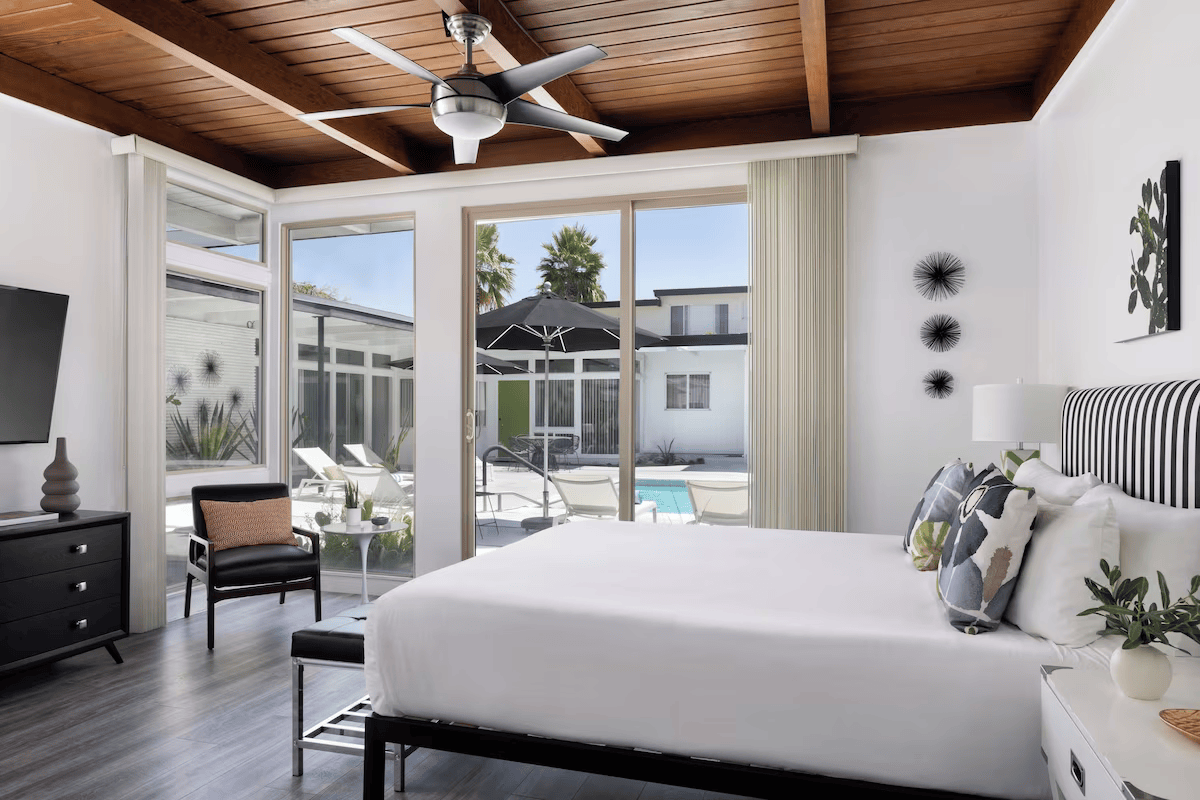 Bright bedroom with a large bed, open balcony doors, pool view, and a ceiling fan under a wood-paneled ceiling