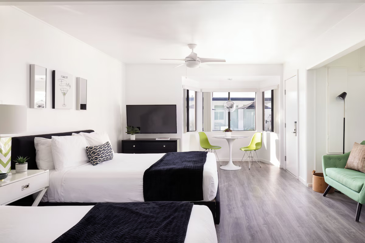 Bright modern studio with white bed, TV, green chairs, and balcony view