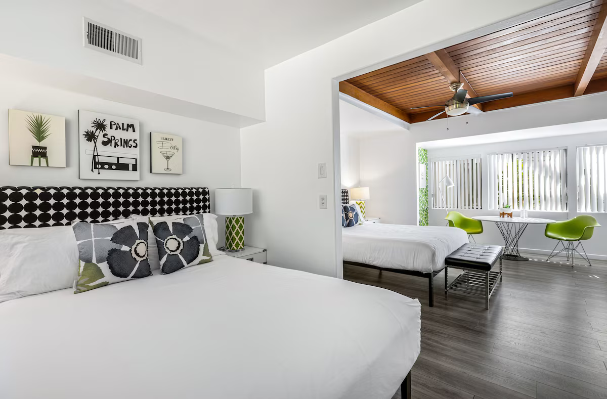 Bright white bedroom with bed, black-and-white pillows, and sitting area opening to a sunny patio