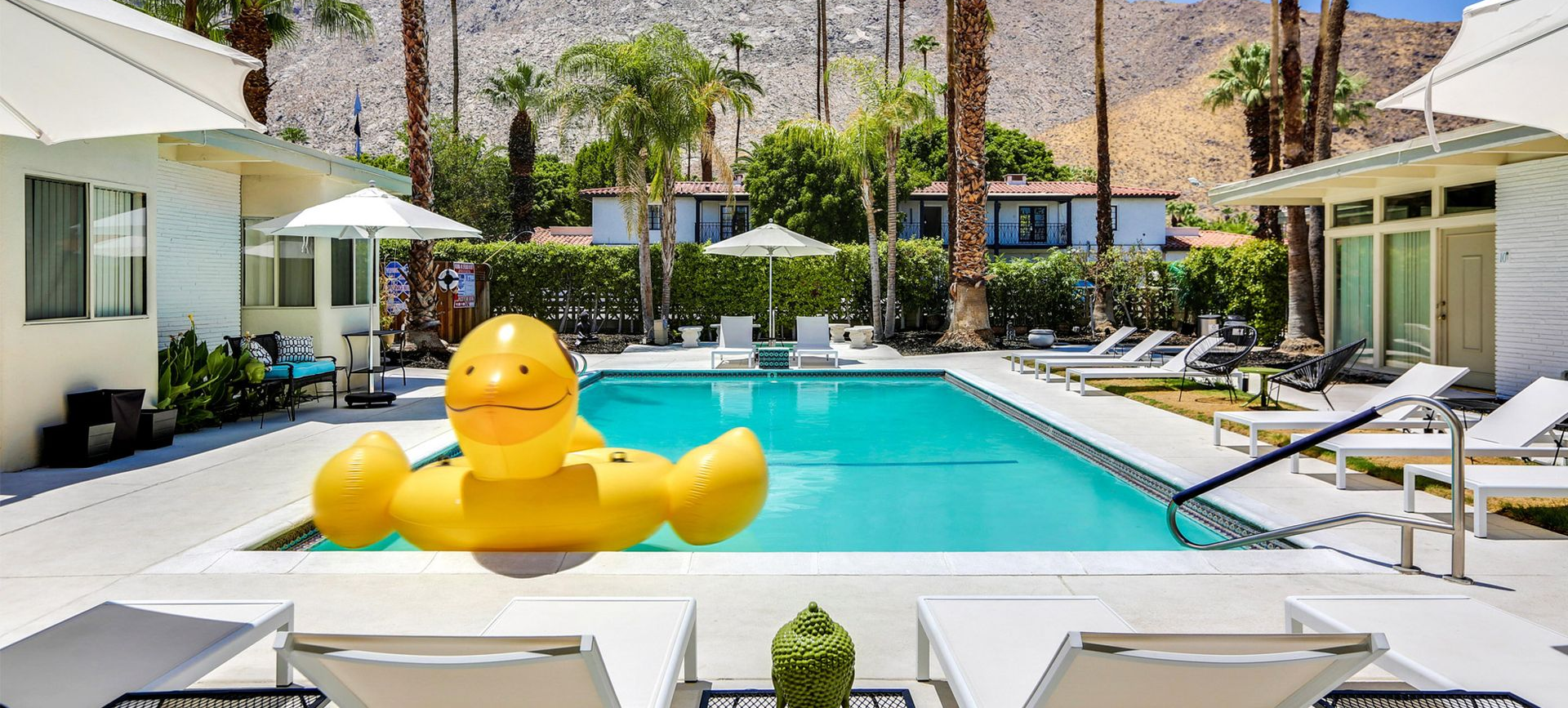 Sunny resort pool with a giant yellow duck float and lounge chairs beside the water