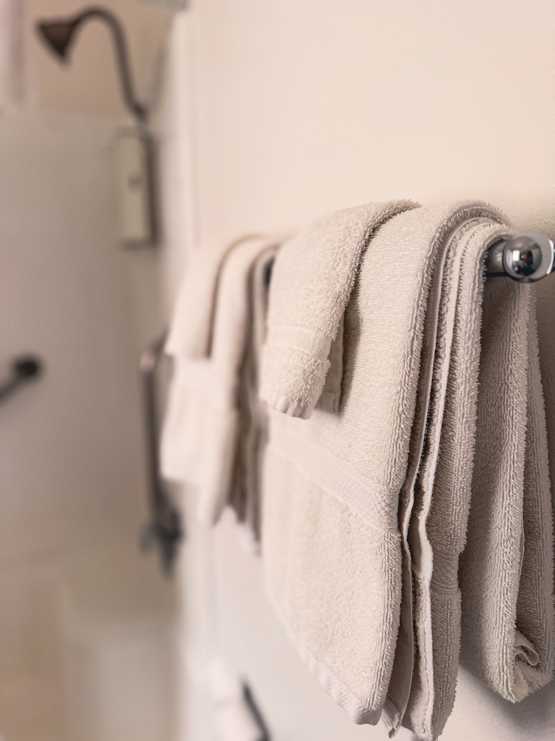 Folded beige towels hanging on a bathroom towel rack.