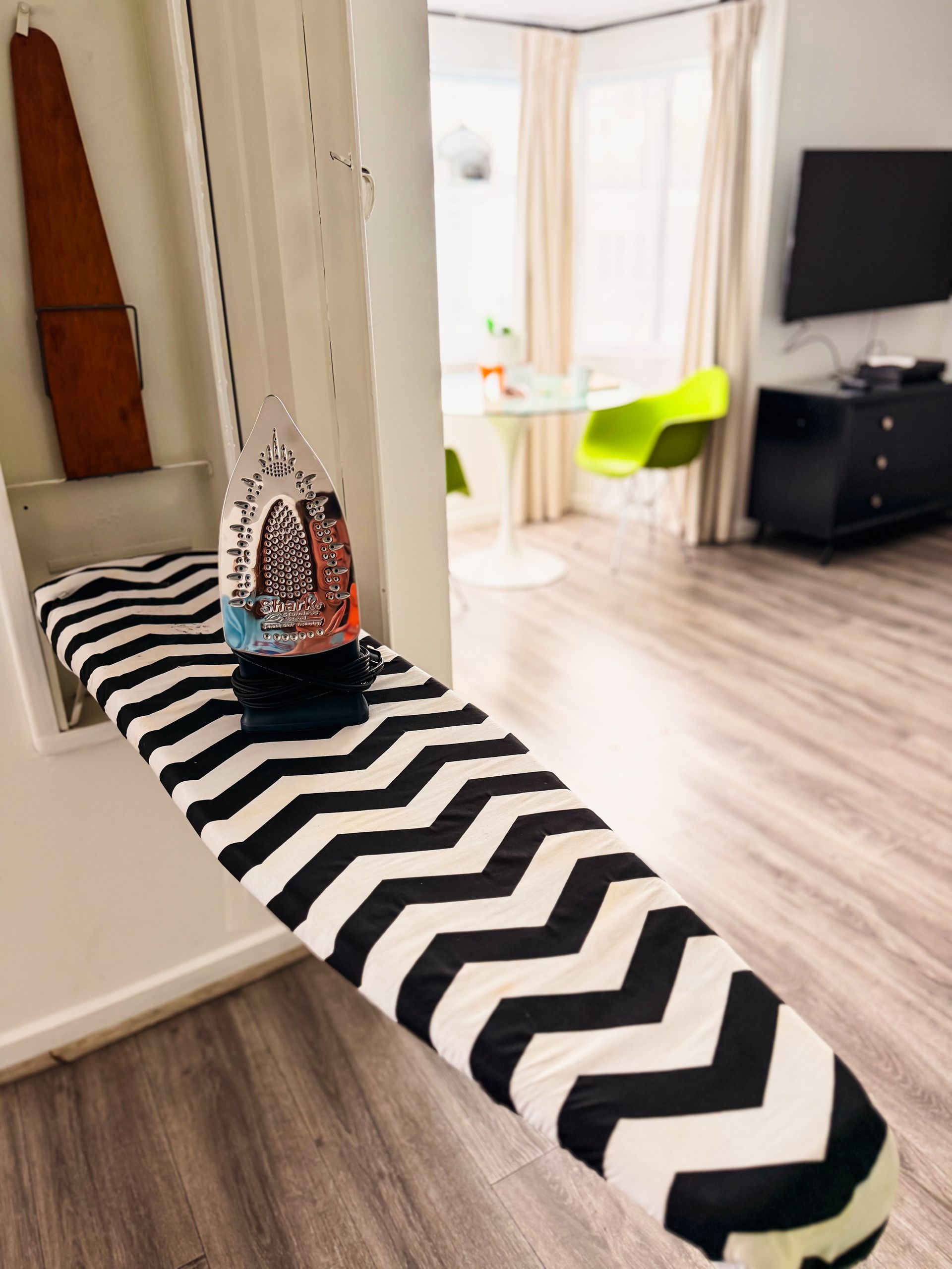 Black-and-white chevron ironing board in a bright room with a TV and lime-green chair