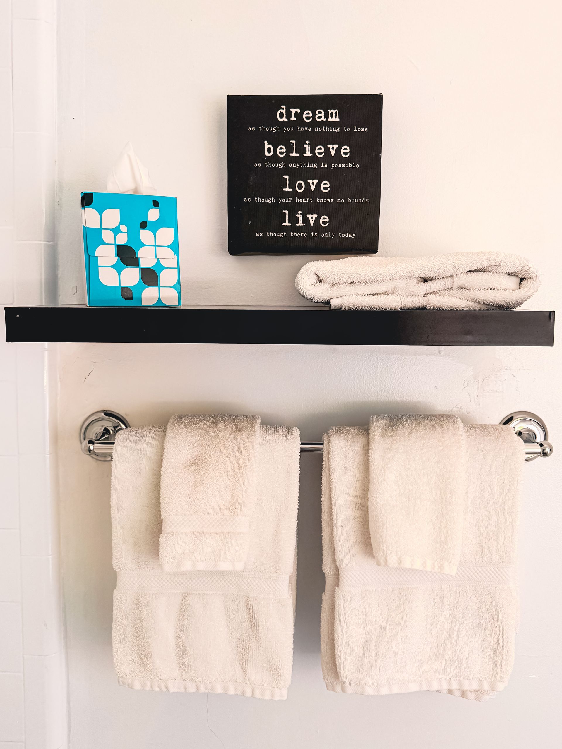 Bathroom shelf with towels, a blue tissue box, and a decorative sign above a towel bar