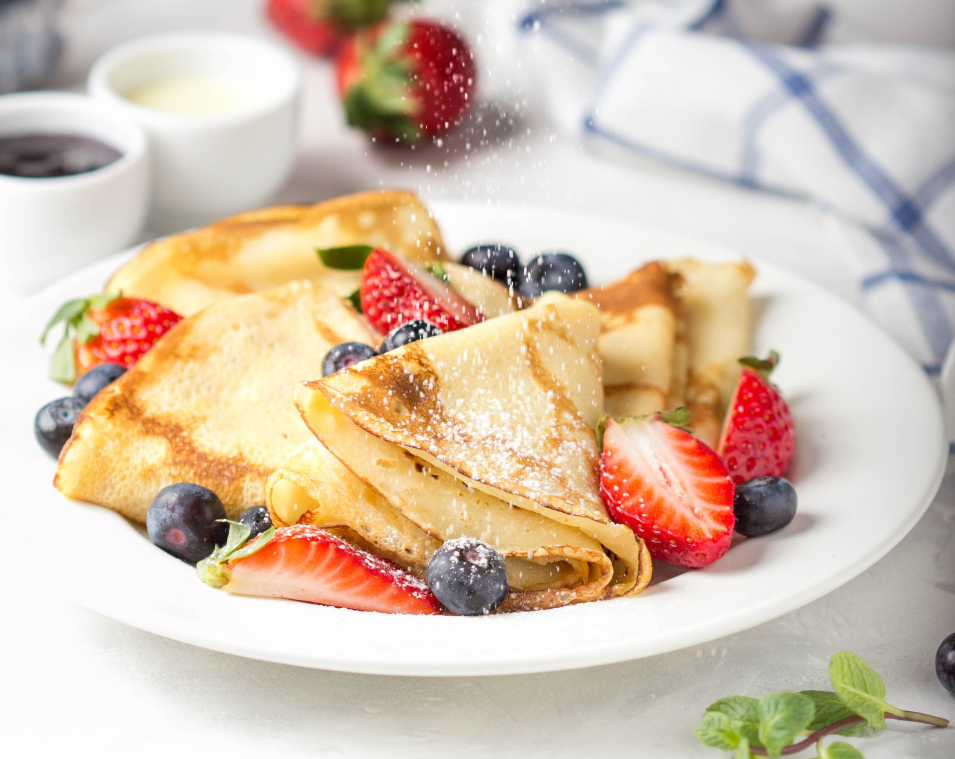 Plate of crepes topped with strawberries, blueberries, and powdered sugar on a breakfast table