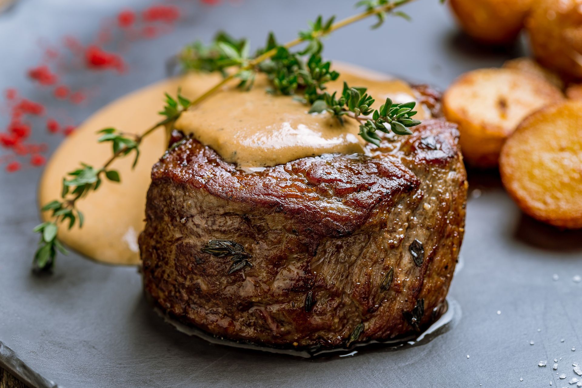 Seared filet mignon topped with sauce and thyme, served with roasted potatoes on a gray plate