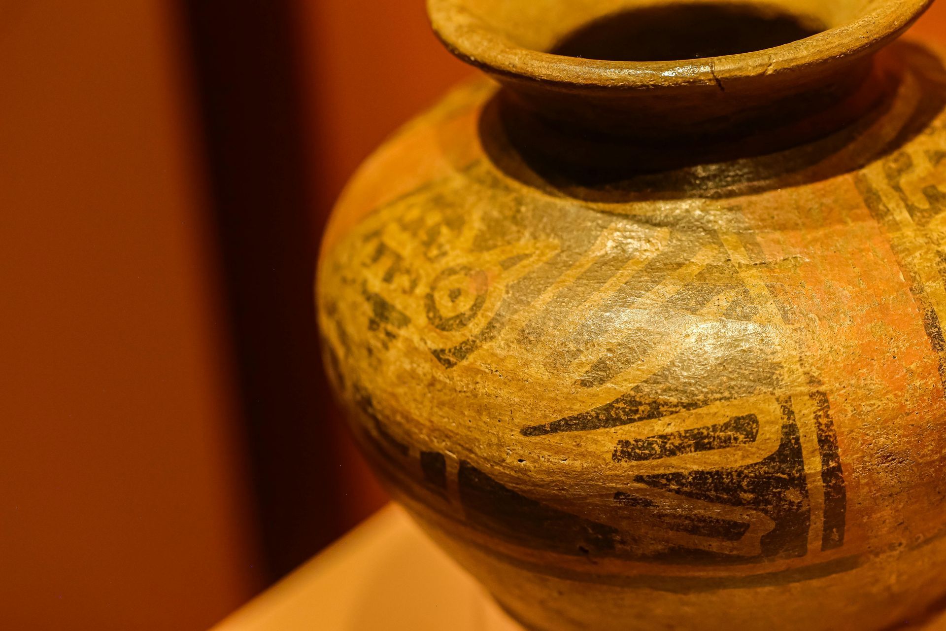 Close-up of a decorated tan ceramic pot with black patterns on a warm orange background