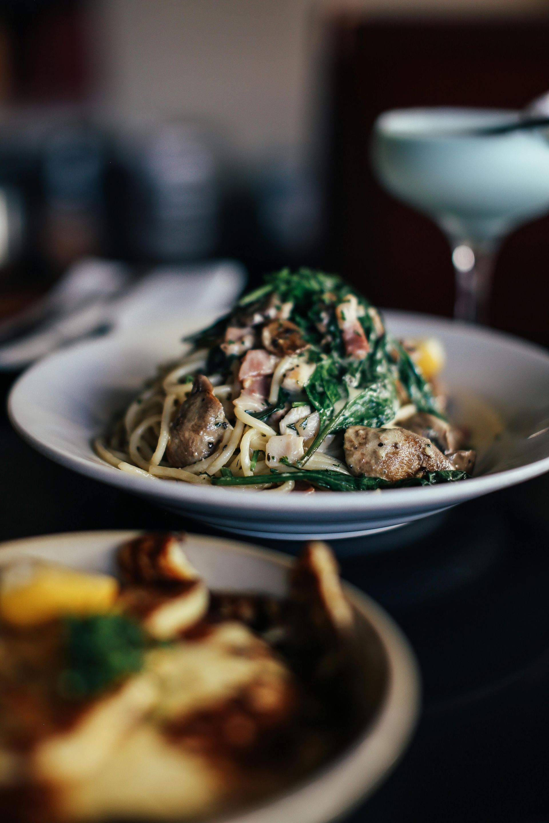 A plated pasta dish topped with herbs and cheese on a dimly lit restaurant table.