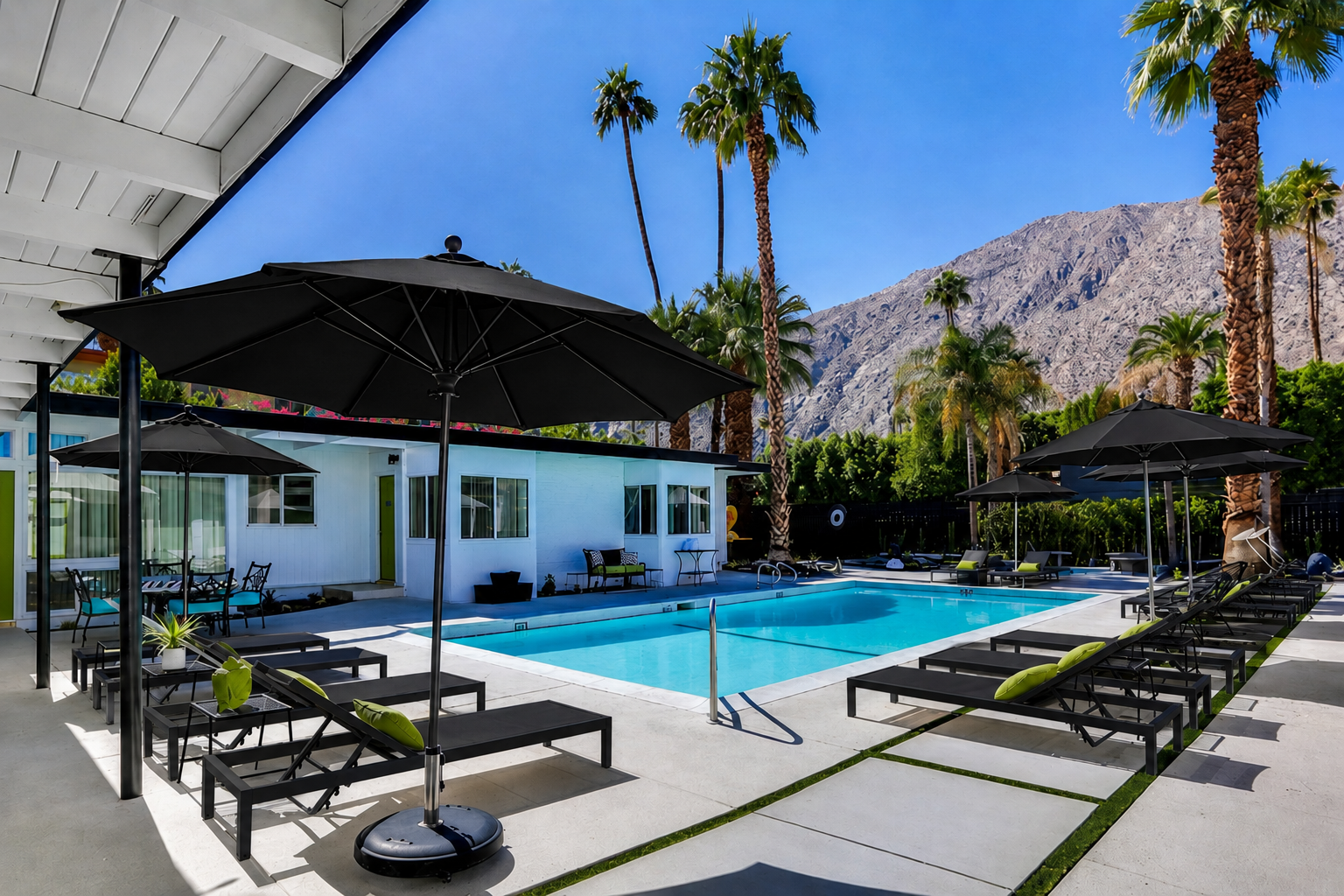Modern pool patio with black loungers, umbrellas, palm trees, and mountain backdrop