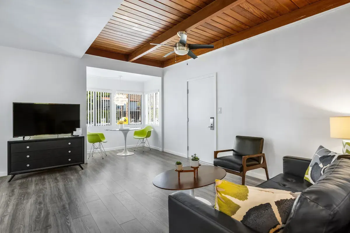 Bright modern living room with gray sofa, TV, chairs, and wood ceiling details