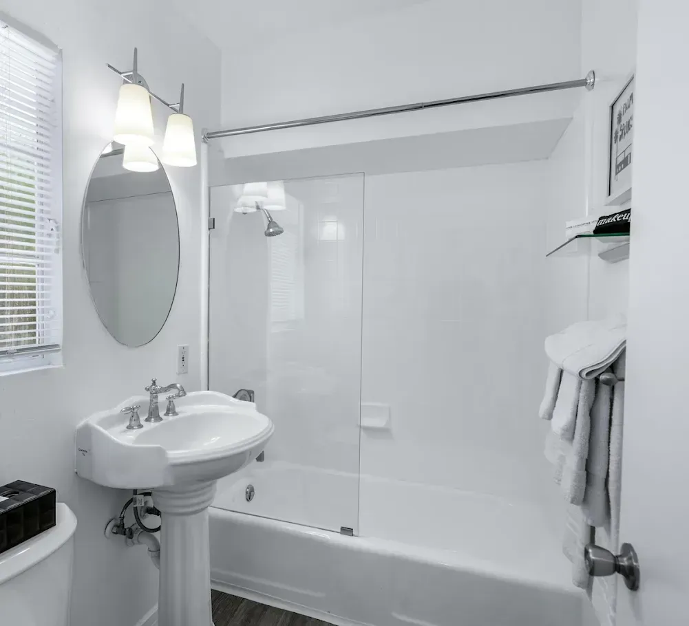 Bright white bathroom with pedestal sink, mirror, tub-shower, and towel rack