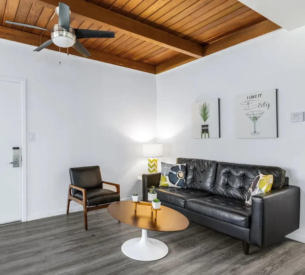Modern living room with black sofa, wooden chair, white walls, wood ceiling, and round coffee table