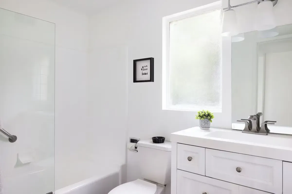 Bright white bathroom with vanity, toilet, mirror, and frosted window