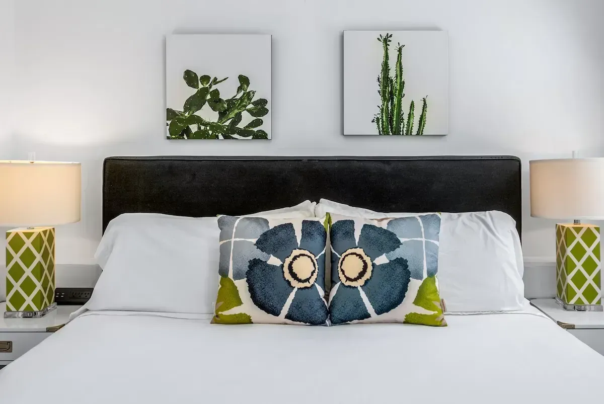 Modern bedroom with white bed, black headboard, green lamps, and botanical wall art
