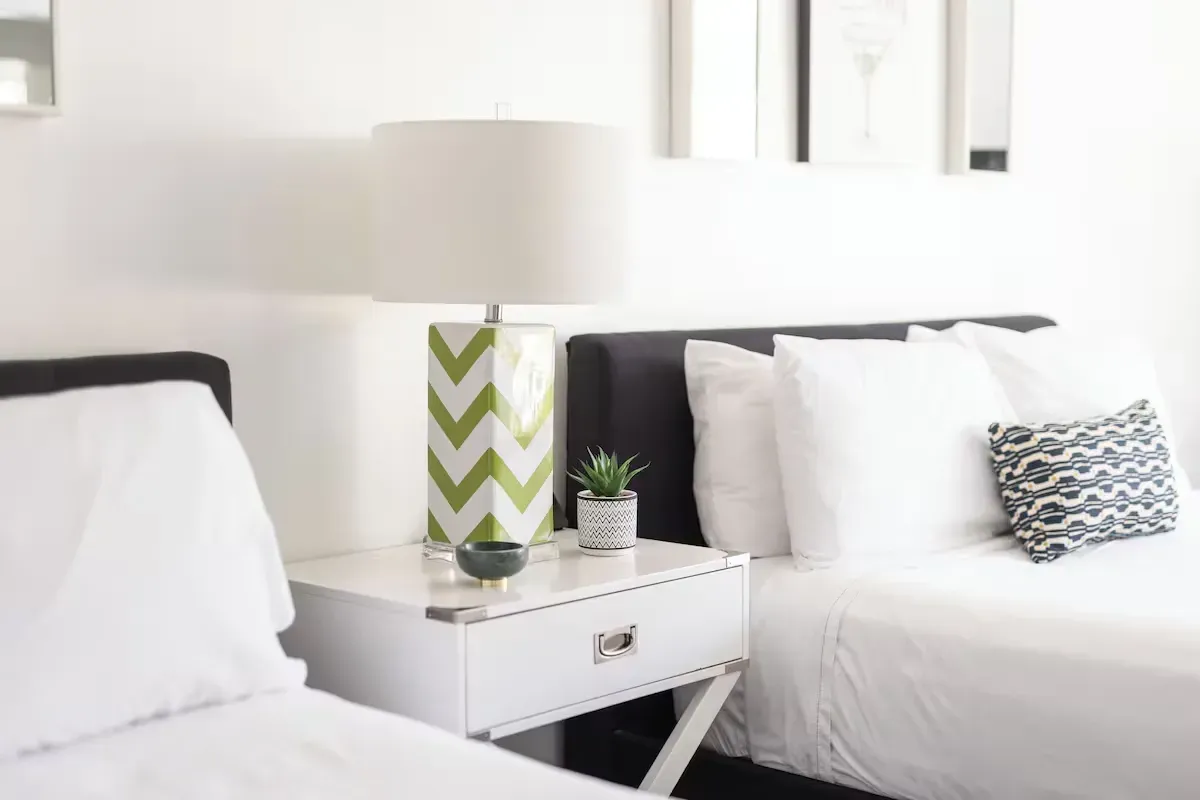 Bright bedroom with two white beds, a chevron lamp, and a small nightstand between them