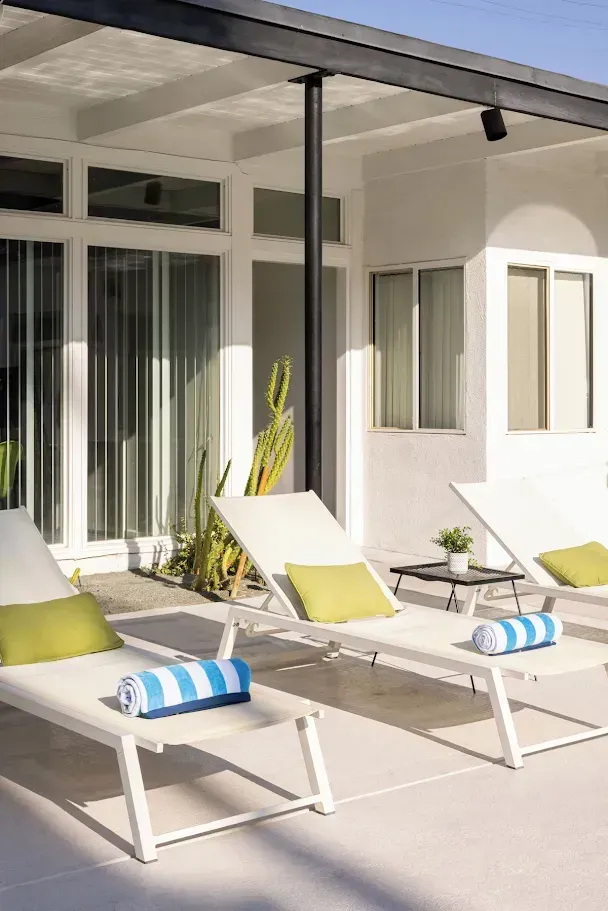 Modern patio with white lounge chairs, lime and blue cushions, and sliding glass doors under a pergola.